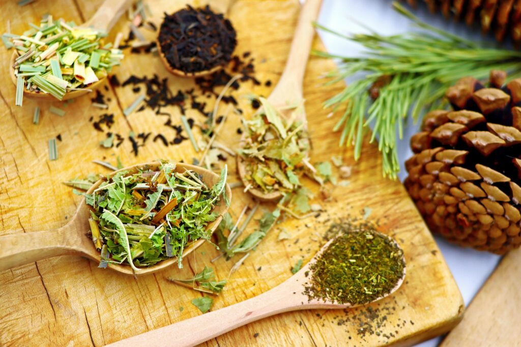 A variety of herbal teas displayed on wooden spoons, set against a rustic wooden board with pine cones.
