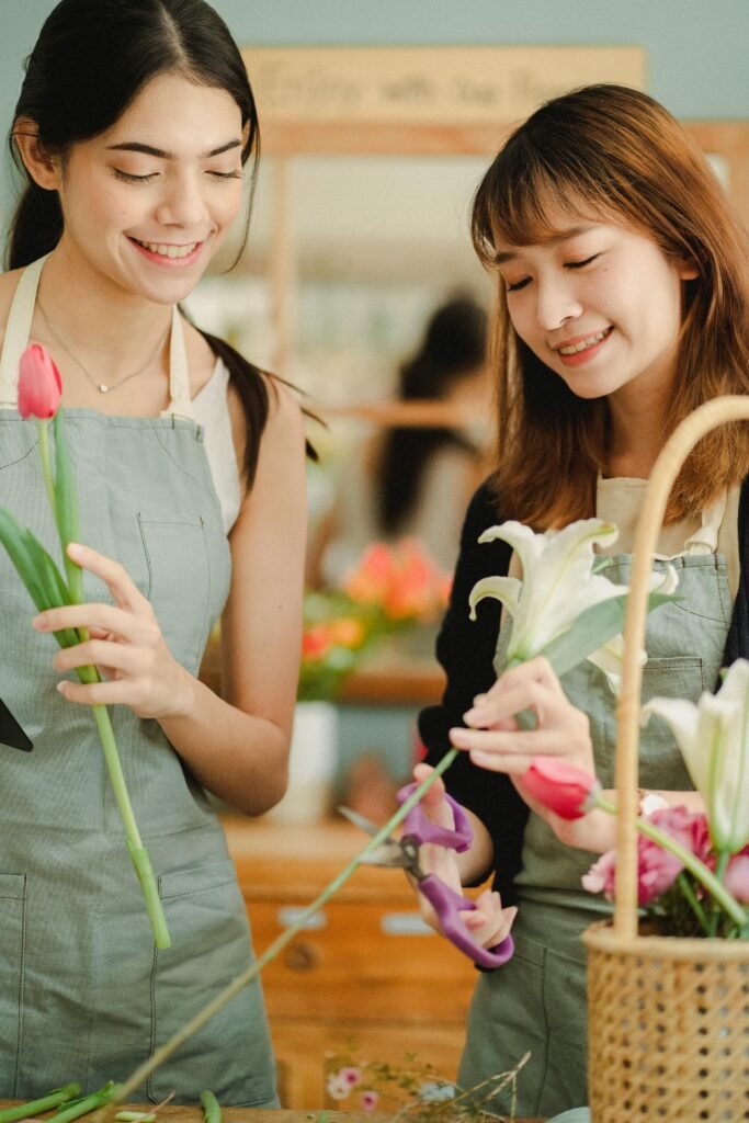 Smiling florists in casual clothes and aprons making composition with fresh flowers while spending time at workshop